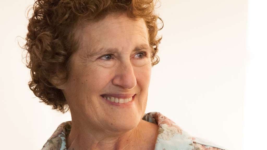 A woman with curly hair smiles warmly at the camera.